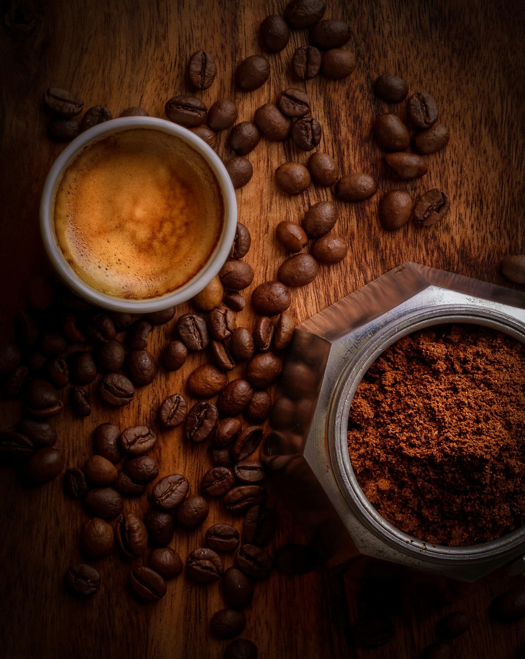 graine_de_cafe_sur_table_avec_cafetière_et_cafe_moulu_et_tasse_de_cafe